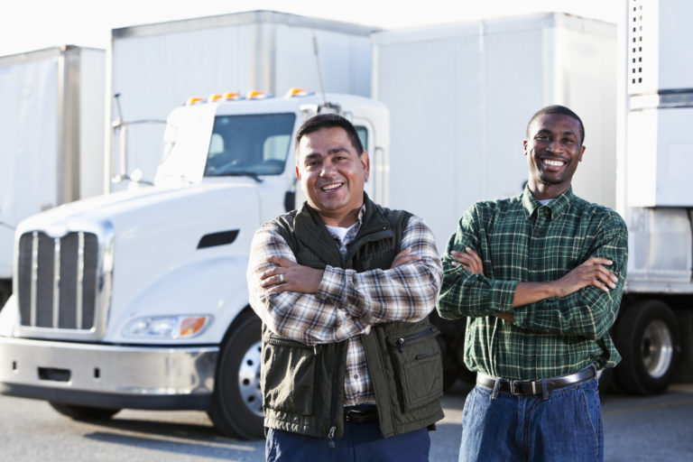 Two men standing in front of 2 of a white semi-truck.